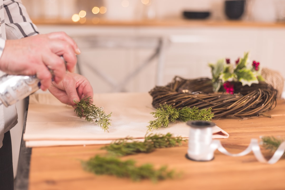 Woman needleworker spray artificial snow on a fir branch doing handmade wreath for Christmas.